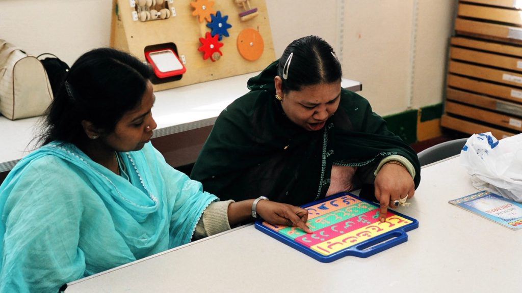 Charity worker helping a learner with disabilities use a tactile alphabet board at a table