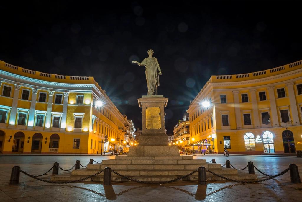 Monument to Duc de Richelieu at night in Odesa, flanked by illuminated yellow semicircular buildings