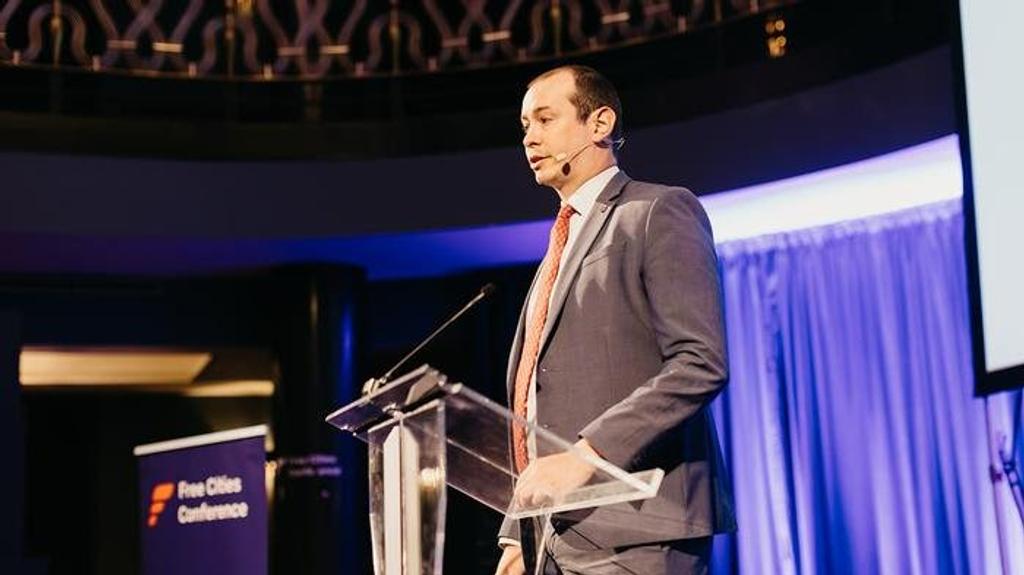 Alex Voss speaking at a lectern on stage at the Free Cities Conference