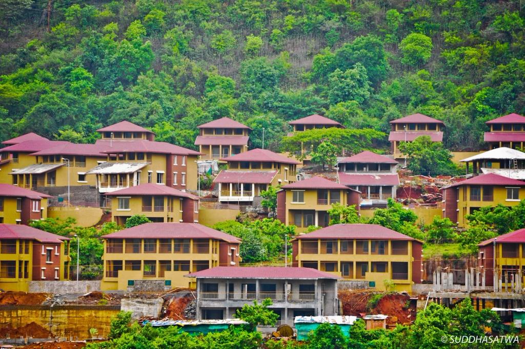Yellow houses with red roofs climbing a green hillside in Lavasa, India's private hill city