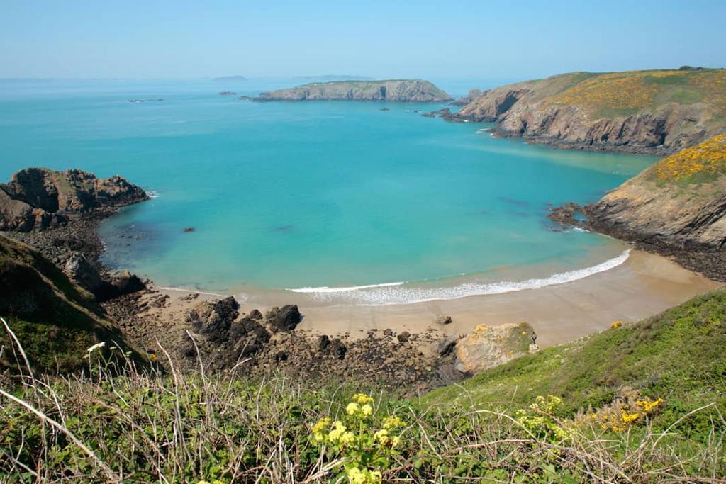 Sandy cove with turquoise water between green headlands on Sark