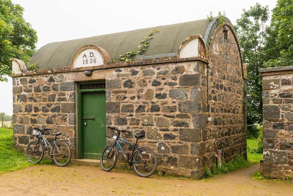 Small granite building dated 1856 with a green door and bicycles parked outside on Sark