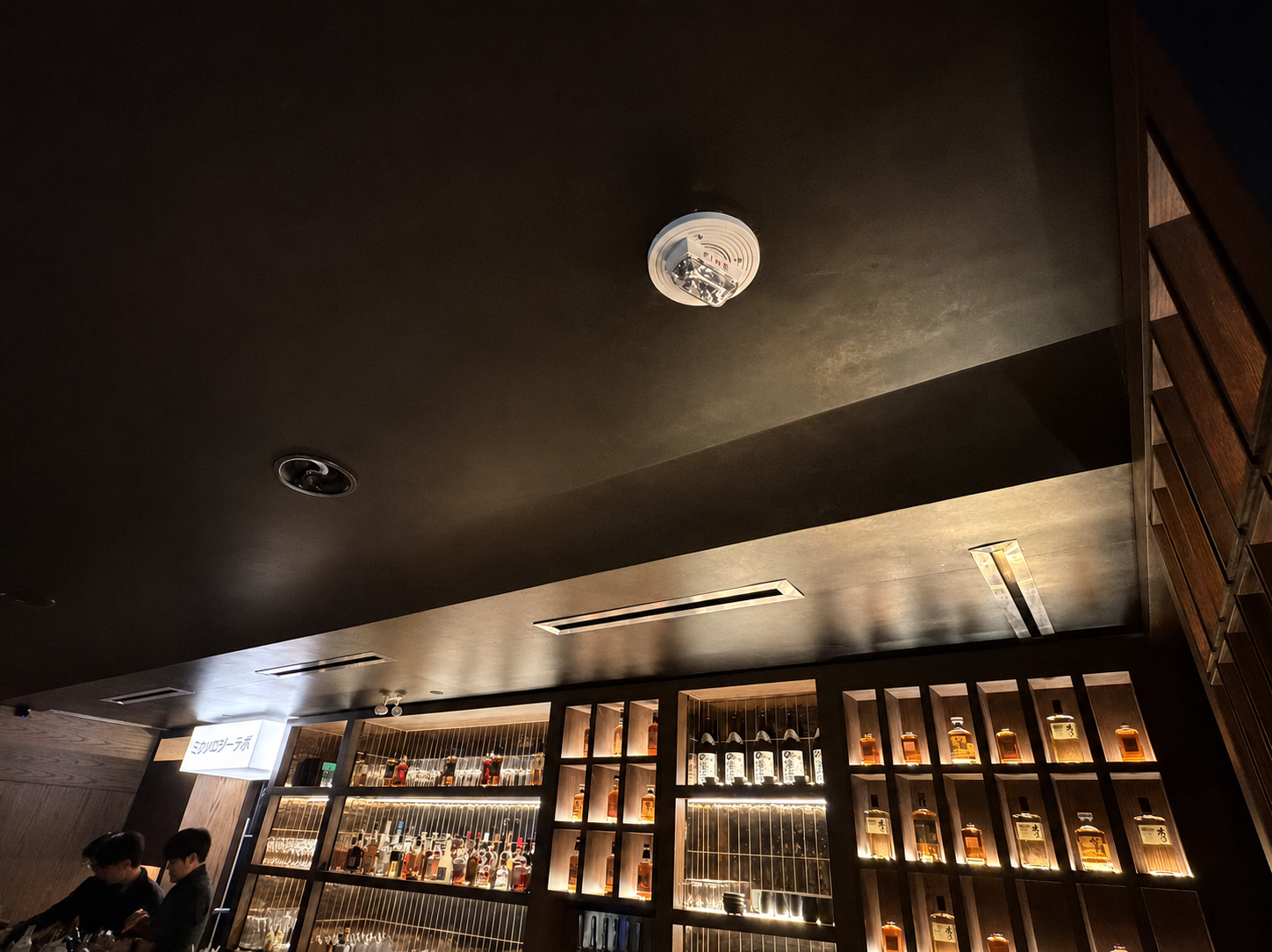 Dark matte ceiling wrap above illuminated whisky bar shelving