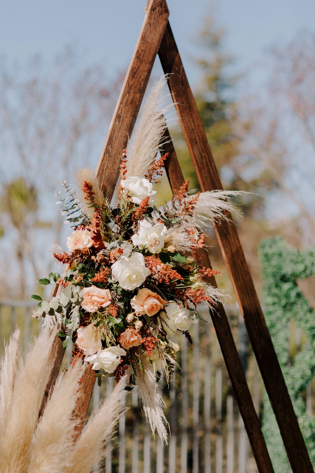 Elegant wedding ceremony arch decorated with white roses, peach florals, dried pampas grass, and natural greenery.