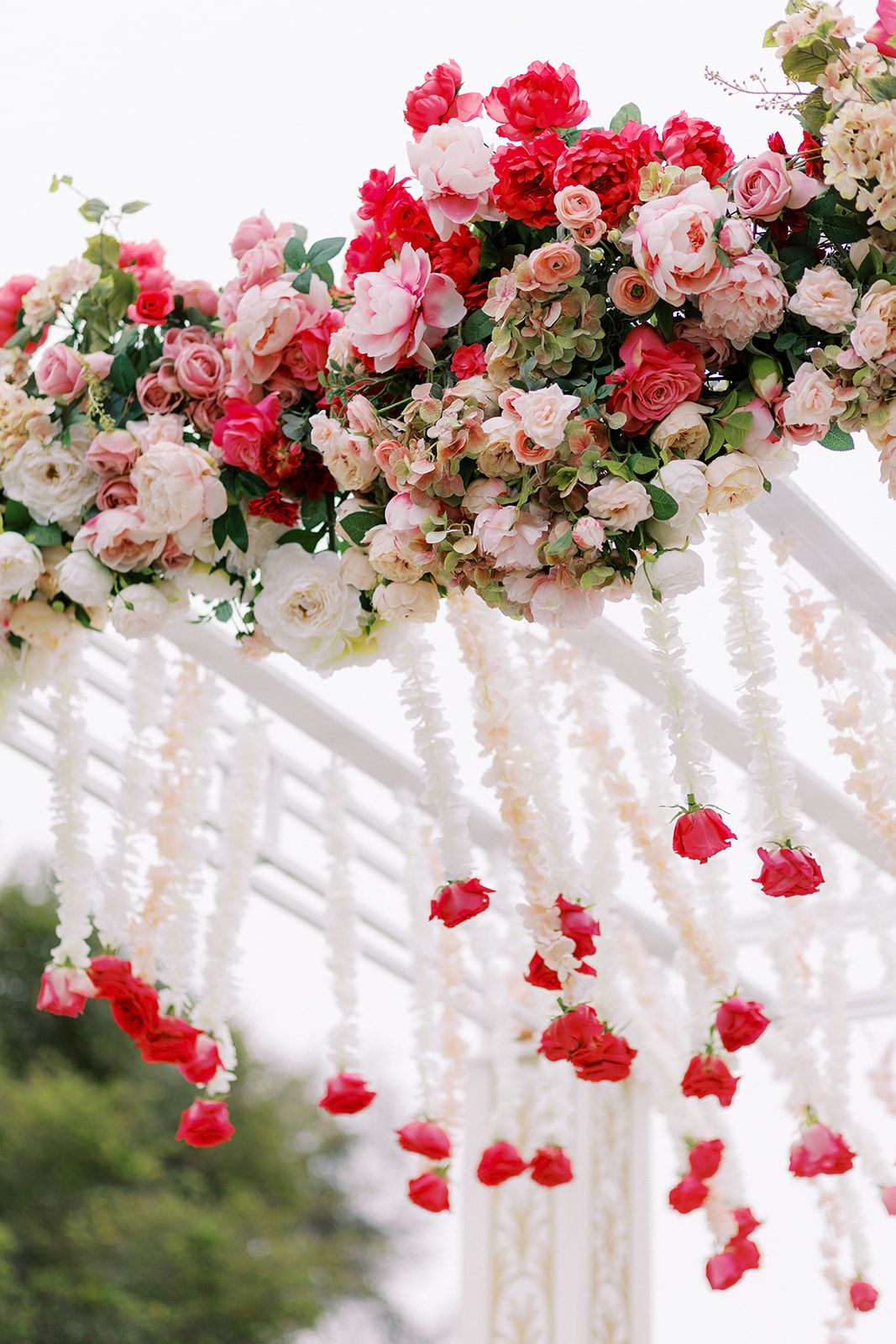 Elegant wedding ceremony arch adorned with pink and red floral arrangements, cascading hanging flowers, and romantic outdoor décor.