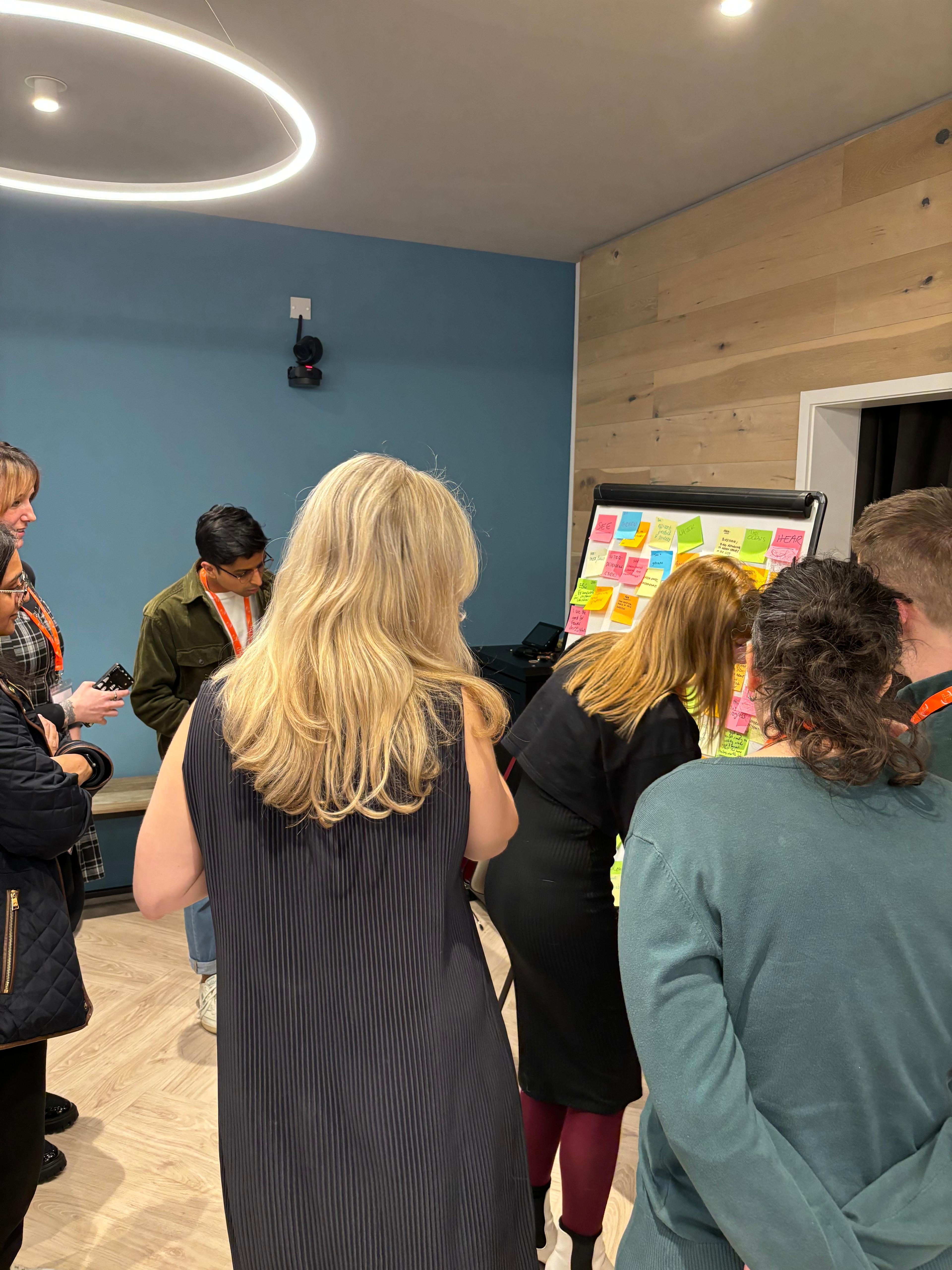 People crowding around a whiteboard with sticky notes on it