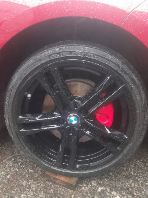A gloss black BMW wheel with a red brake caliper, on a red BMW 2 Series Gran Coupé