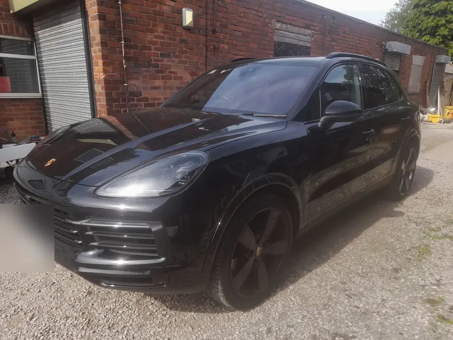 A black Porsche Cayenne on gloss black wheels, outside the workshop