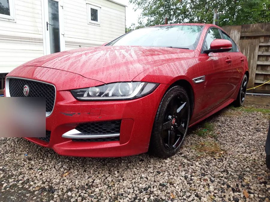 A red Jaguar XE on gloss black wheels, on the gravel yard