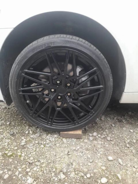 A gloss black multi-spoke wheel on a white car