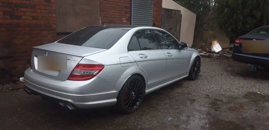 A silver Mercedes C-Class on gloss black wheels, seen from behind