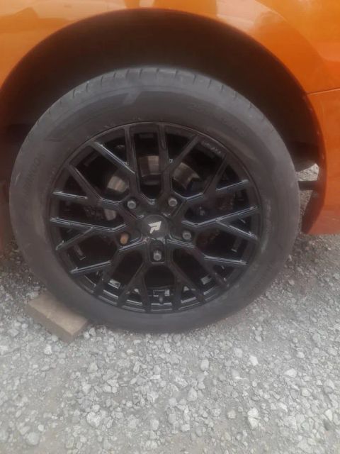 A gloss black multi-spoke wheel on an orange hatchback
