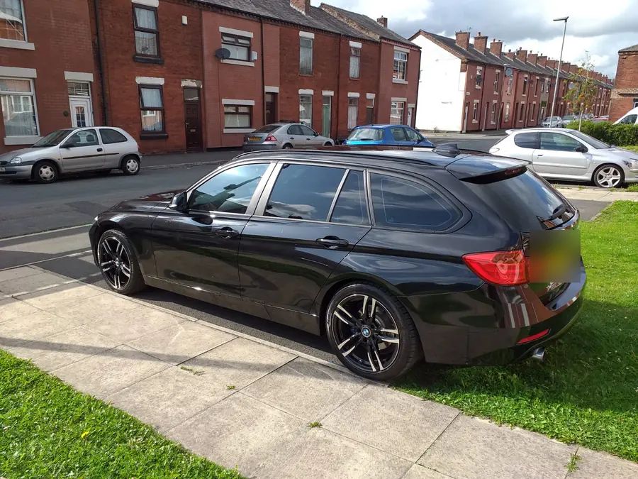 A black BMW 3 Series Touring on black wheels, parked on a street
