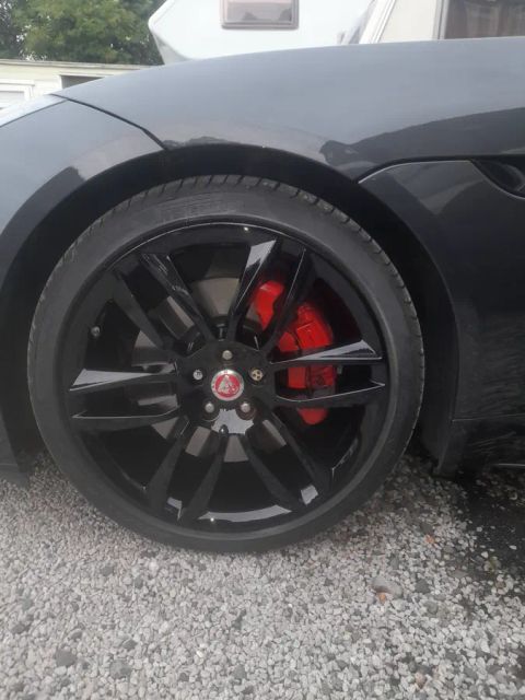 A gloss black wheel with a red brake caliper behind the spokes