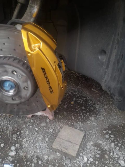 A yellow AMG brake caliper behind a drilled disc