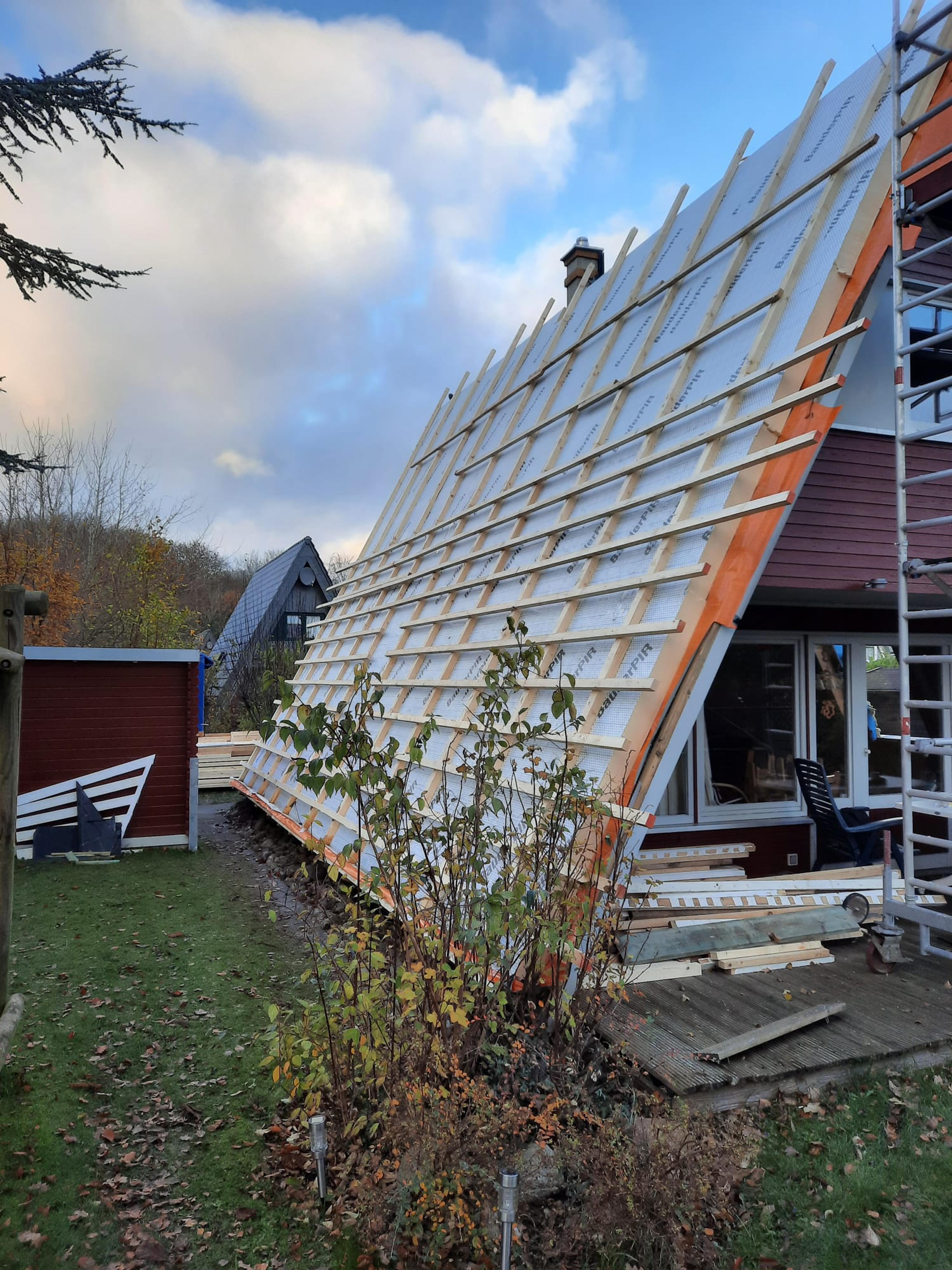 A-förmiges Dach eines Hauses wird renoviert, mit Baugerüst und Holzverstrebungen, Herbstlandschaft.