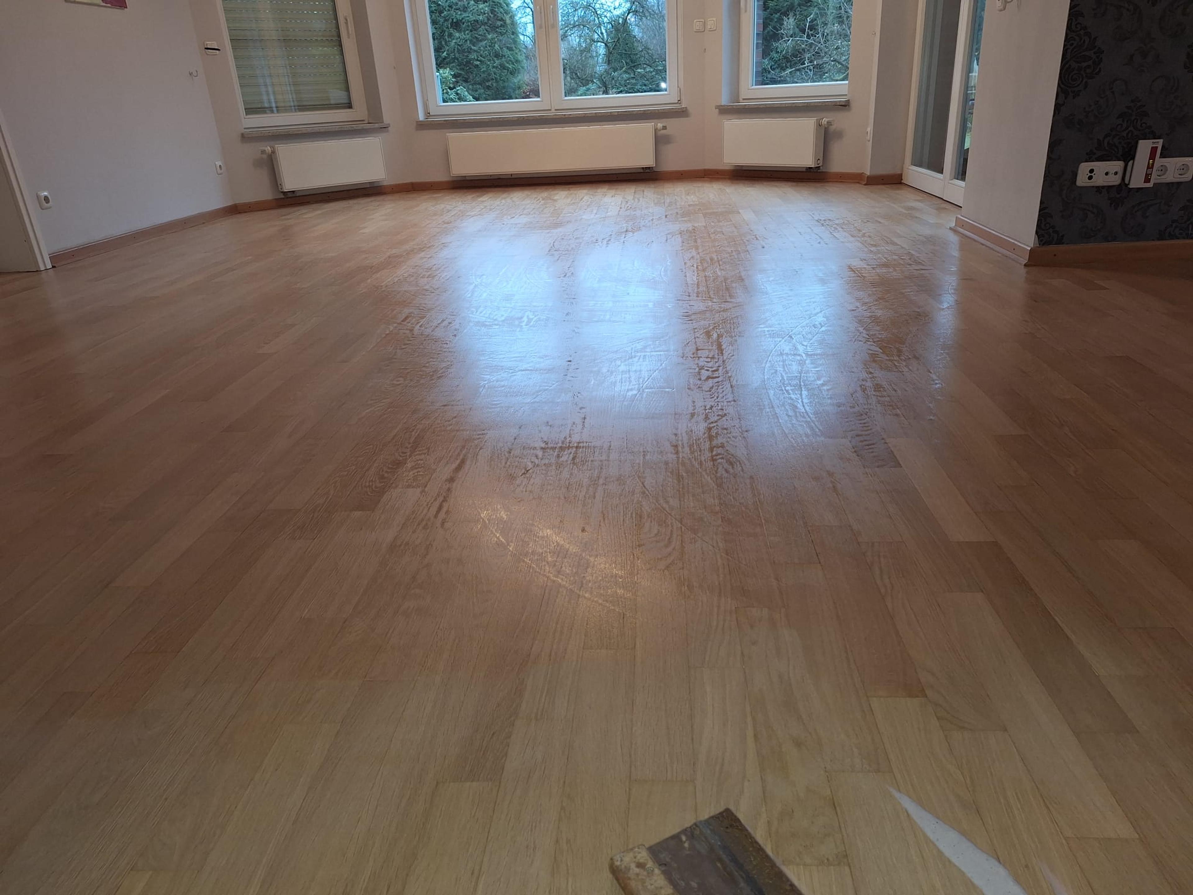 Frisch renovierter Holzboden in einem leeren Raum mit großen Fenstern