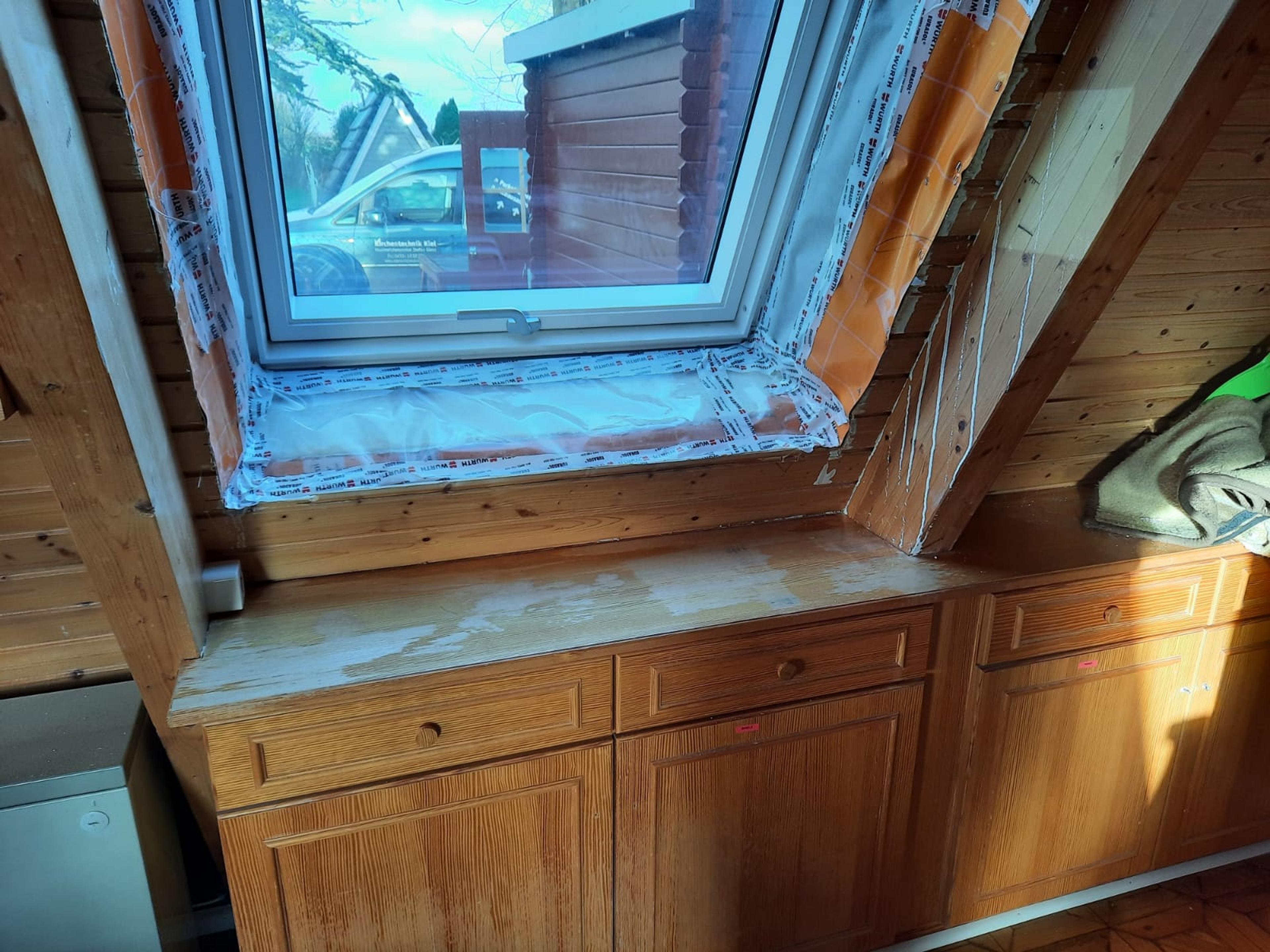 Dachfenster mit Holzvertäfelung, teilweise renoviert, mit Abdichtungsfolie umgeben.