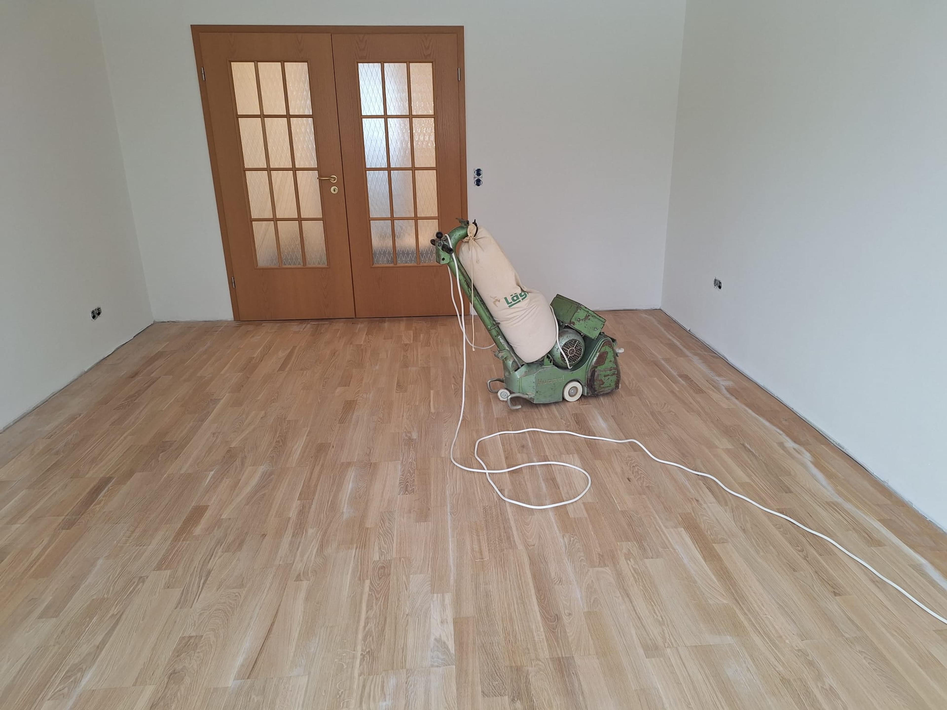 Leerer Raum mit Holzfußboden, Schleifmaschine und verschlossenen Holztüren.