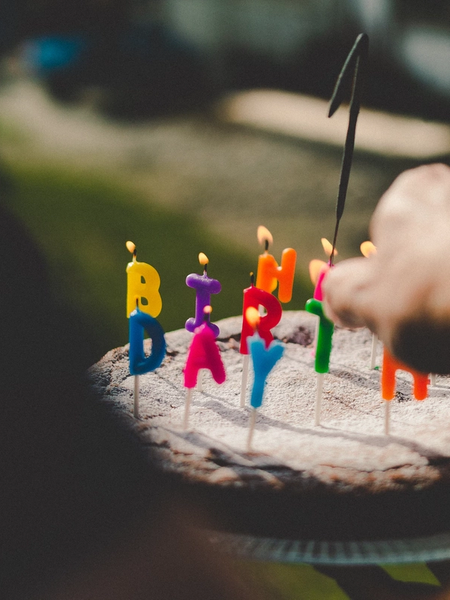 A hand lighting a candle on a cake decorated with letter candles spelling out Happy Birthday