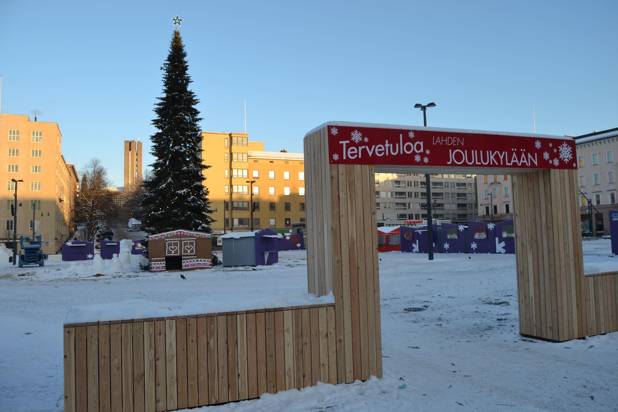Tervetuloa Lahden Joulukylään -portti lumisella torilla, taustalla joulukuusi ja myyntikojuja