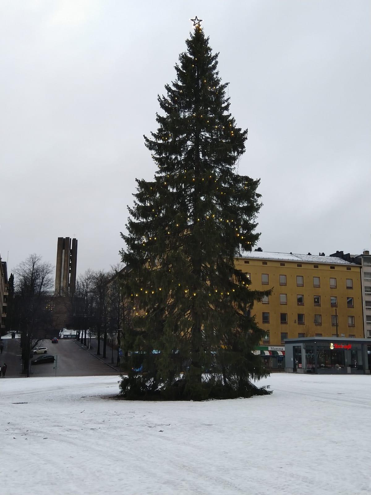 Valoin koristeltu joulukuusi lumisella torilla harmaana talvipäivänä, 24.12.2020