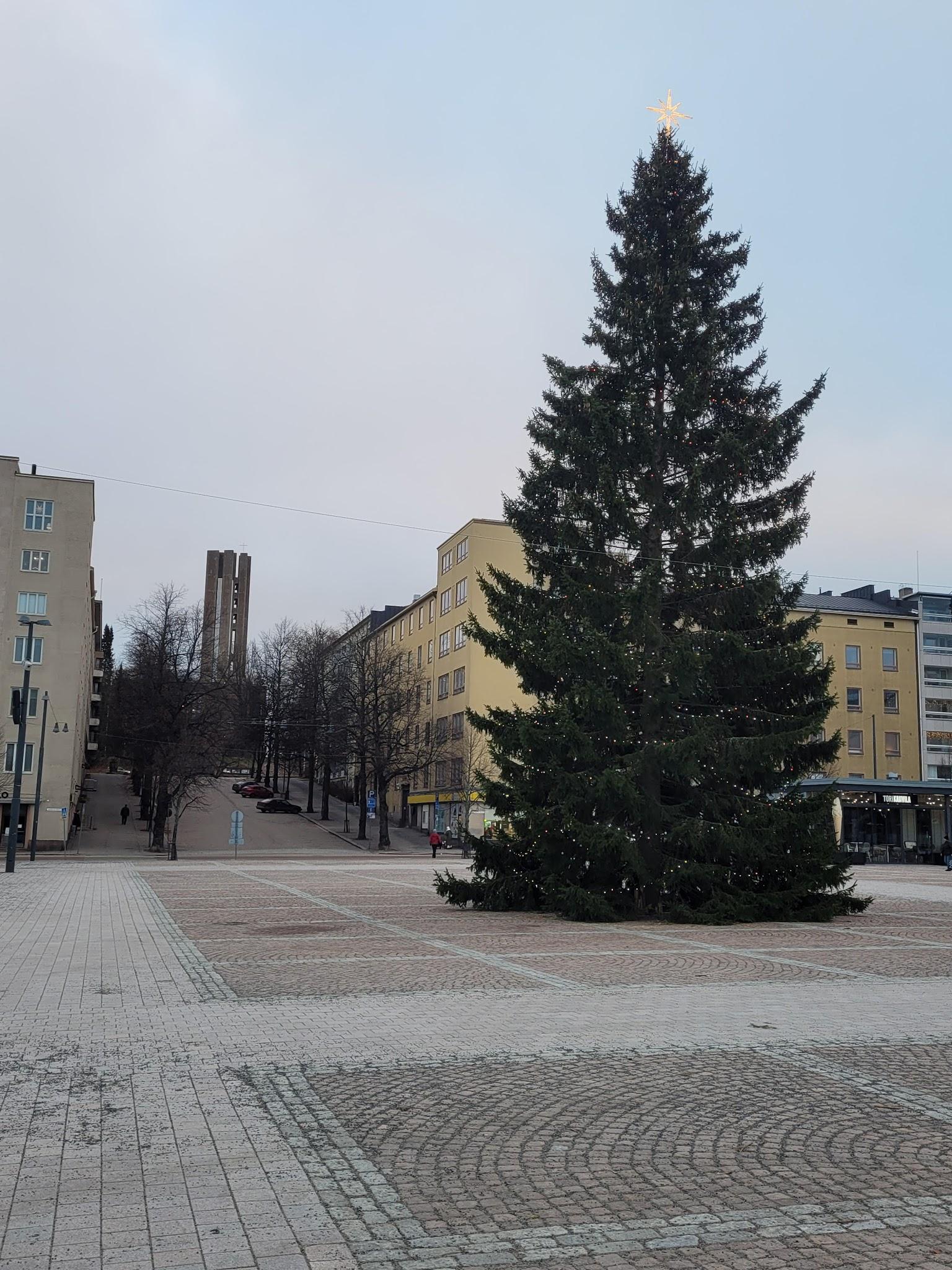 Valoin koristeltu joulukuusi kivetyllä torilla kerrostalojen keskellä, 24.12.2025