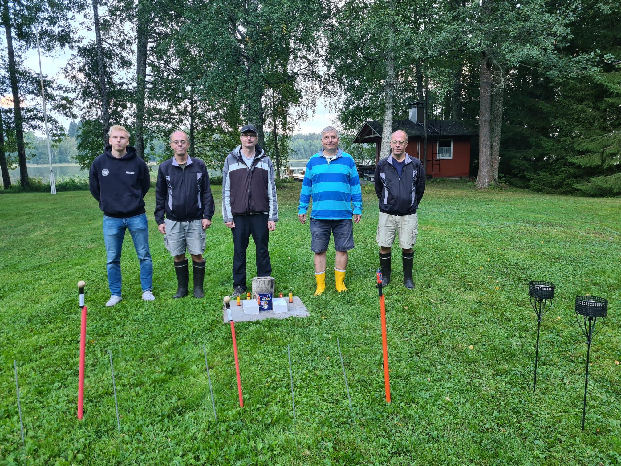 Viisi klubilaista järvenrannan nurmella ilotulitteiden ja tulitelineiden takana, 31.08.2024