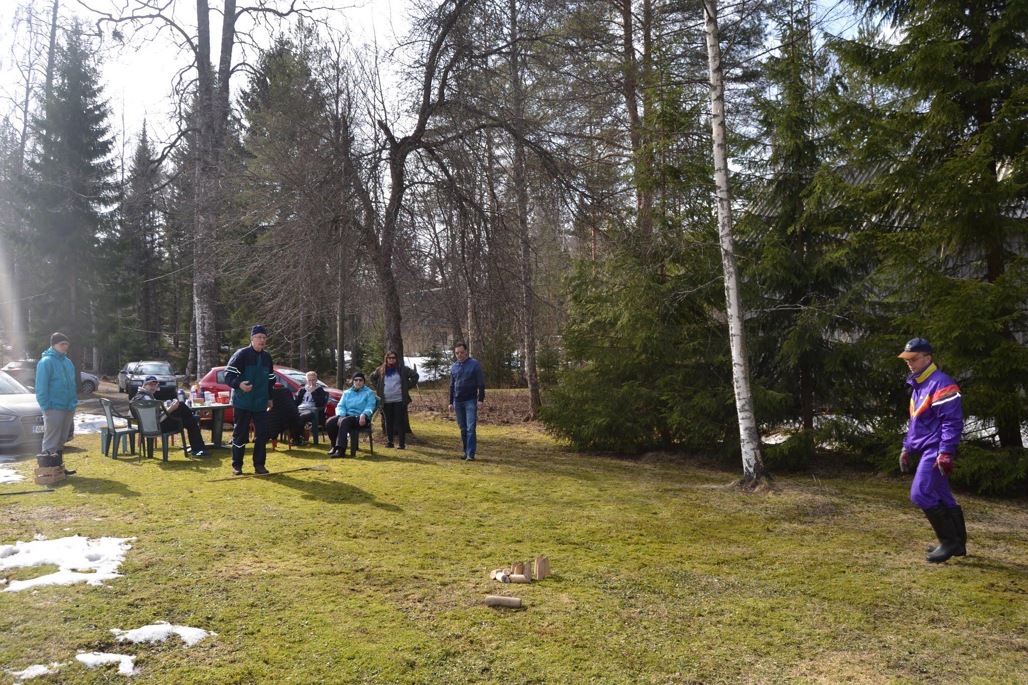 Mölkkypeli käynnissä keväisellä nurmikolla, pelaaja violetissa asussa ja katsojia tuoleilla, 19.04.2019