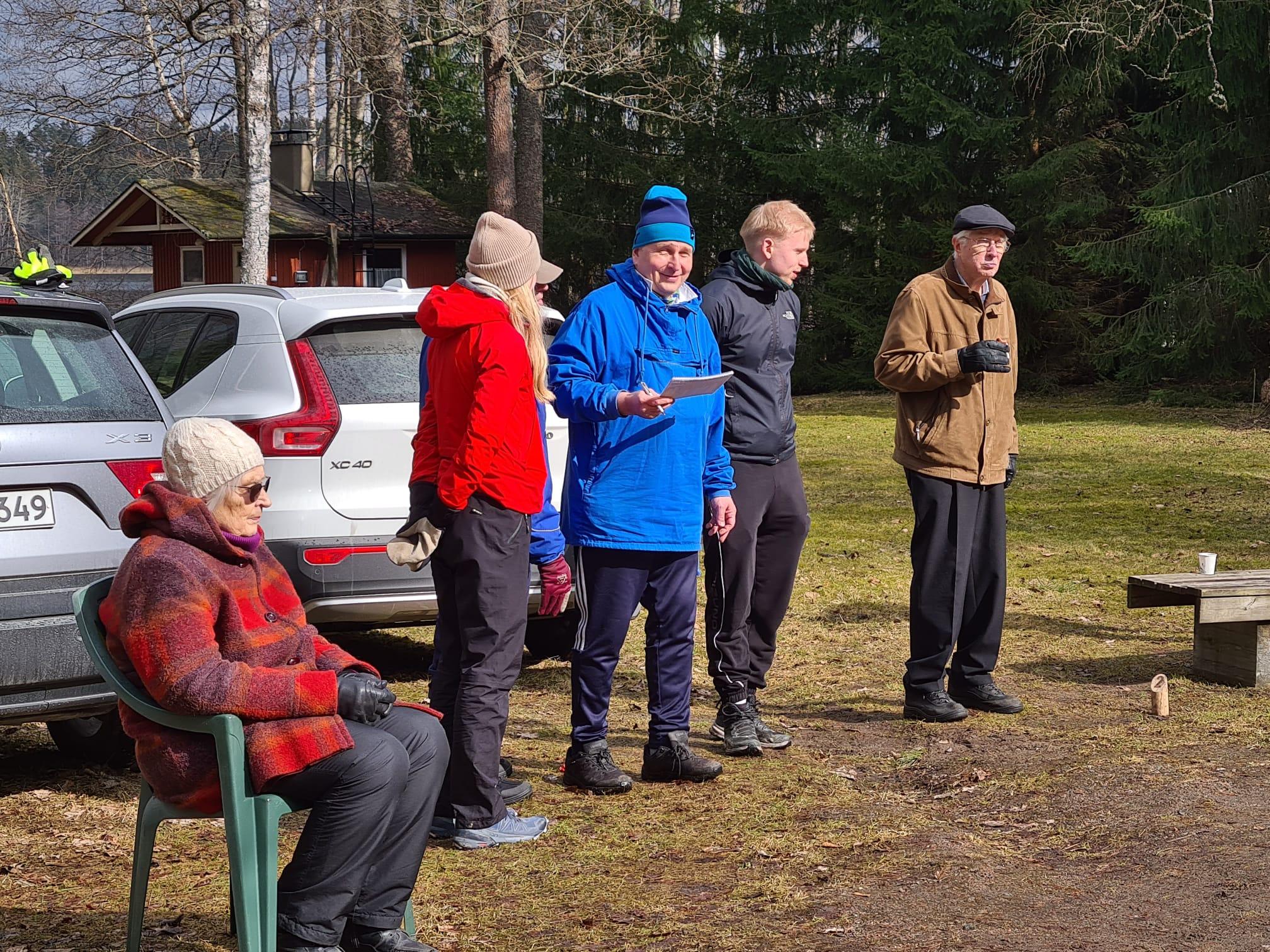 Klubilaiset seuraavat mölkkypeliä pysäköityjen autojen vieressä, yksi pitää pistekirjanpitoa, 05.04.2026