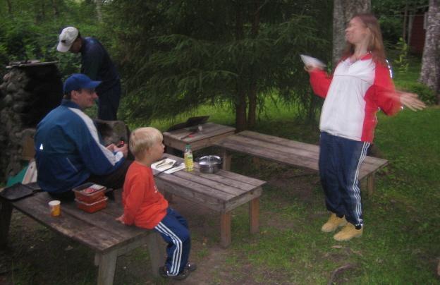 Seurue eväspöytien ääressä metsäisellä grillipaikalla, yksi seisoo heittoasennossa, 06.07.2007