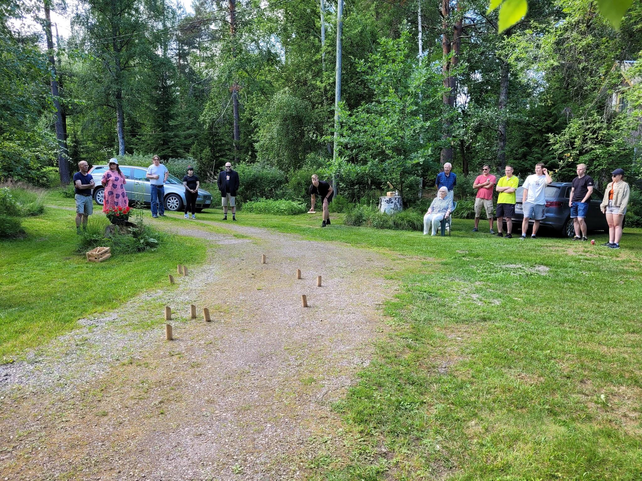 Klubilaisia seuraamassa mölkkyheittoa hiekkatiellä vehreällä pihalla kesäjuhlassa, 15.07.2023
