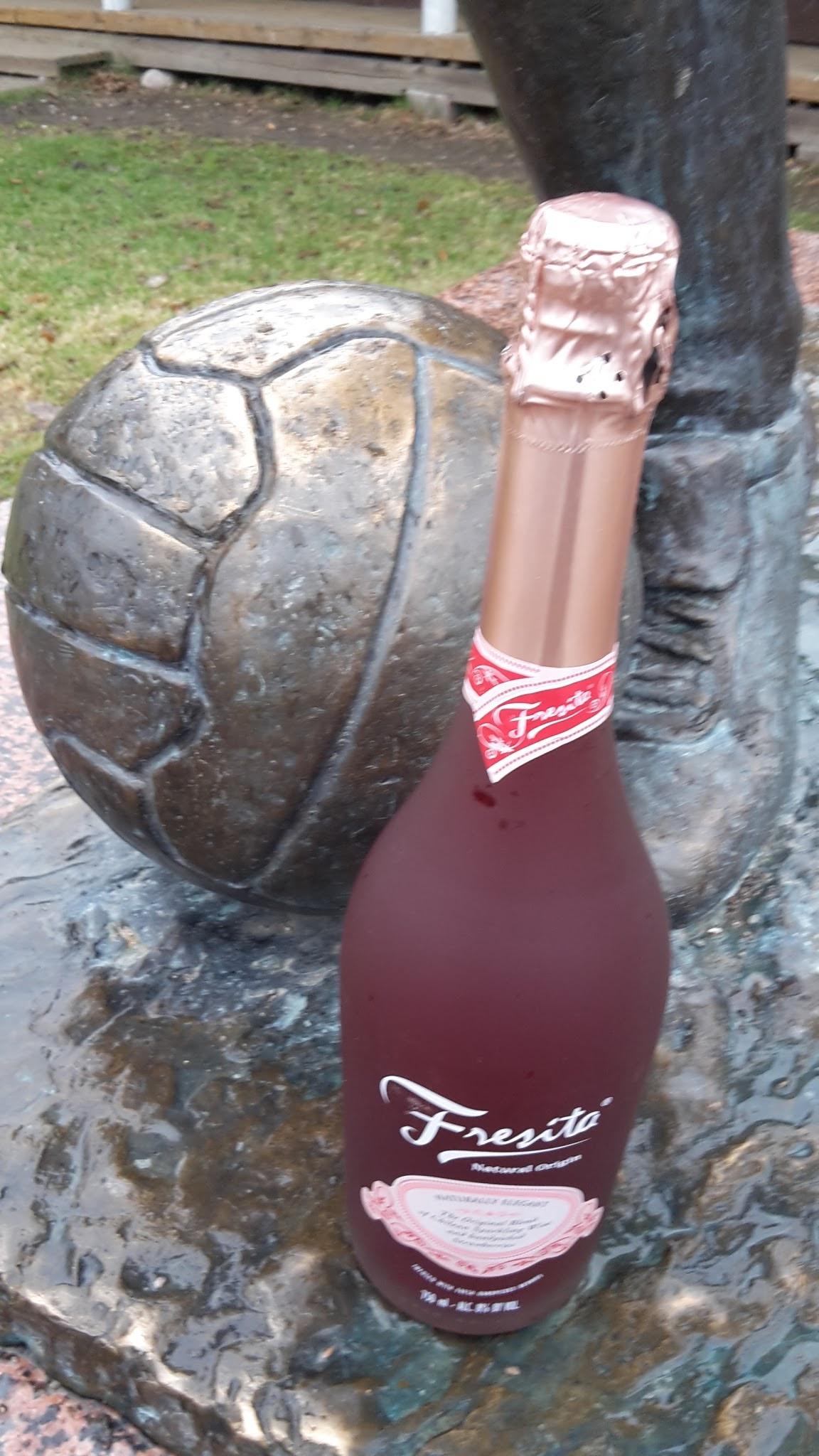 Fresita-kuohuviinipullo jalkapalloilijapatsaan pronssisen pallon ja jalan vieressä vappuna, 01.05.2018