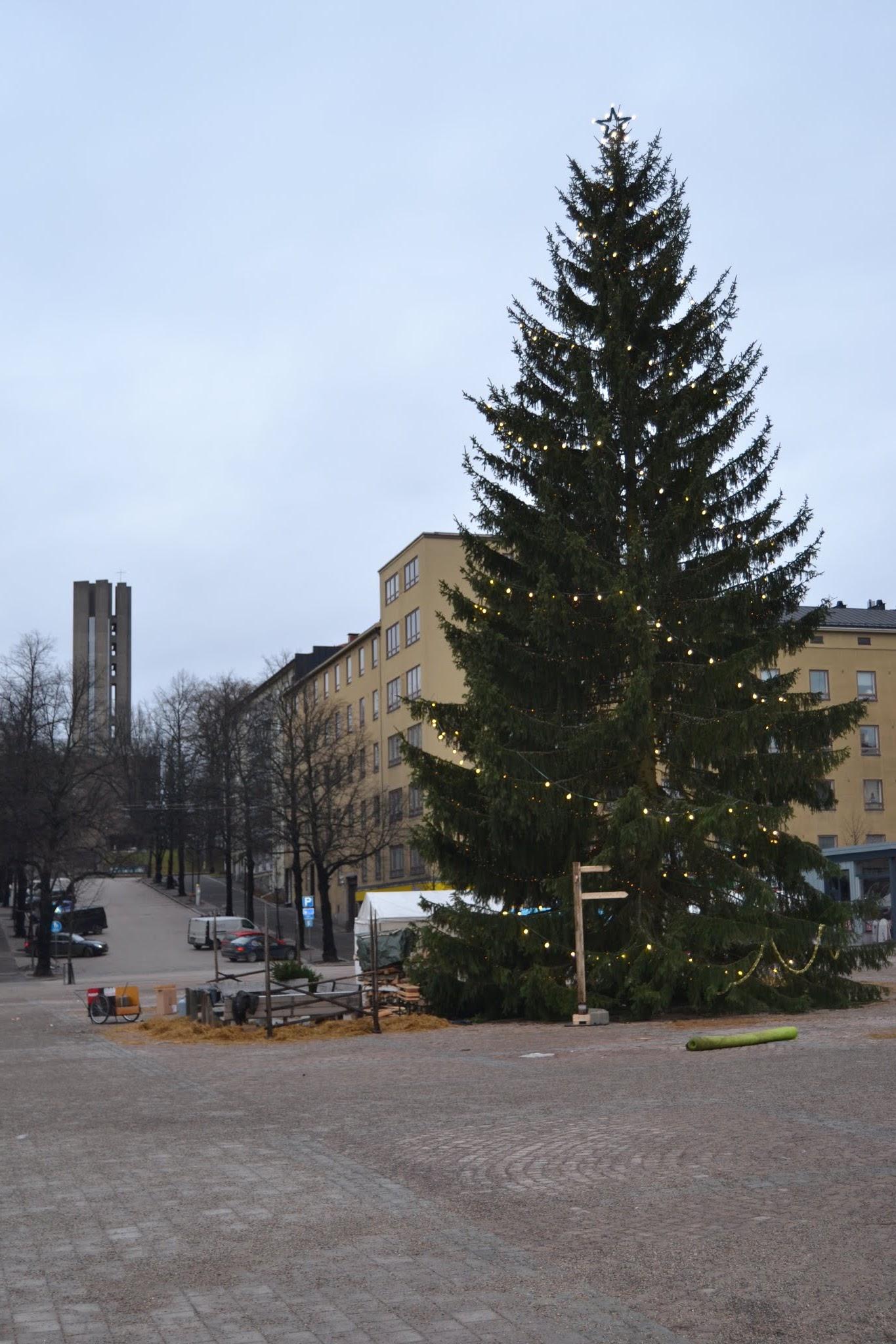 Valoilla ja tähdellä koristeltu joulukuusi Lahden torilla, taustalla keltaisia kerrostaloja ja betonitorni