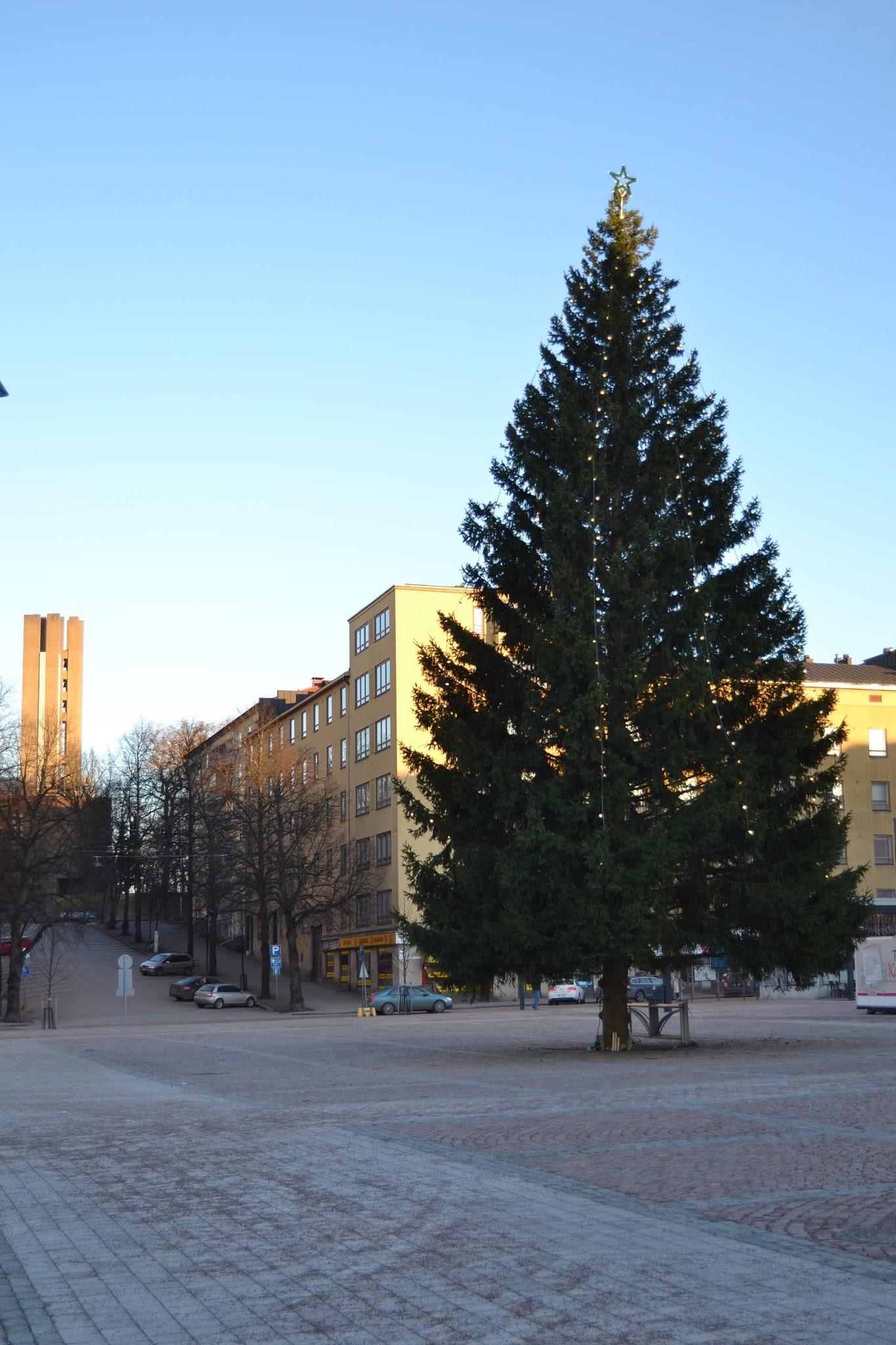Valoilla ja tähdellä koristeltu joulukuusi aurinkoisella Lahden torilla, taustalla kerrostaloja ja betonitorni