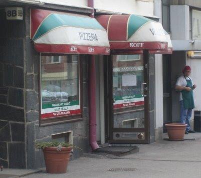 Pizzeria Villetan sisäänkäynti punavihreine markiiseineen ja ovella seisova kokki