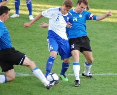 Viro–Suomi-ottelussa Suomen valkopaitainen pelaaja numero 6 pallon kimpussa Viron sinipaitaisten välissä, 21.05.2010