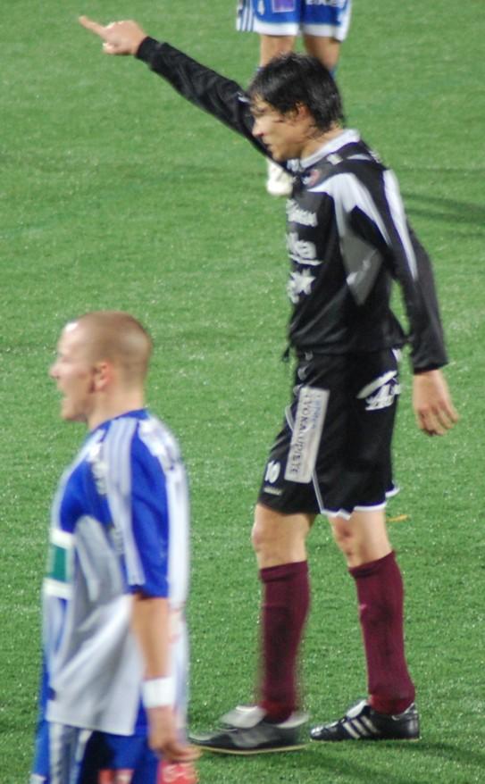 Litmanen tummassa pelipaidassa numerolla 10 osoittaa kädellään kentällä, edessä sinivalkoasuinen vastapelaaja, 26.10.2008
