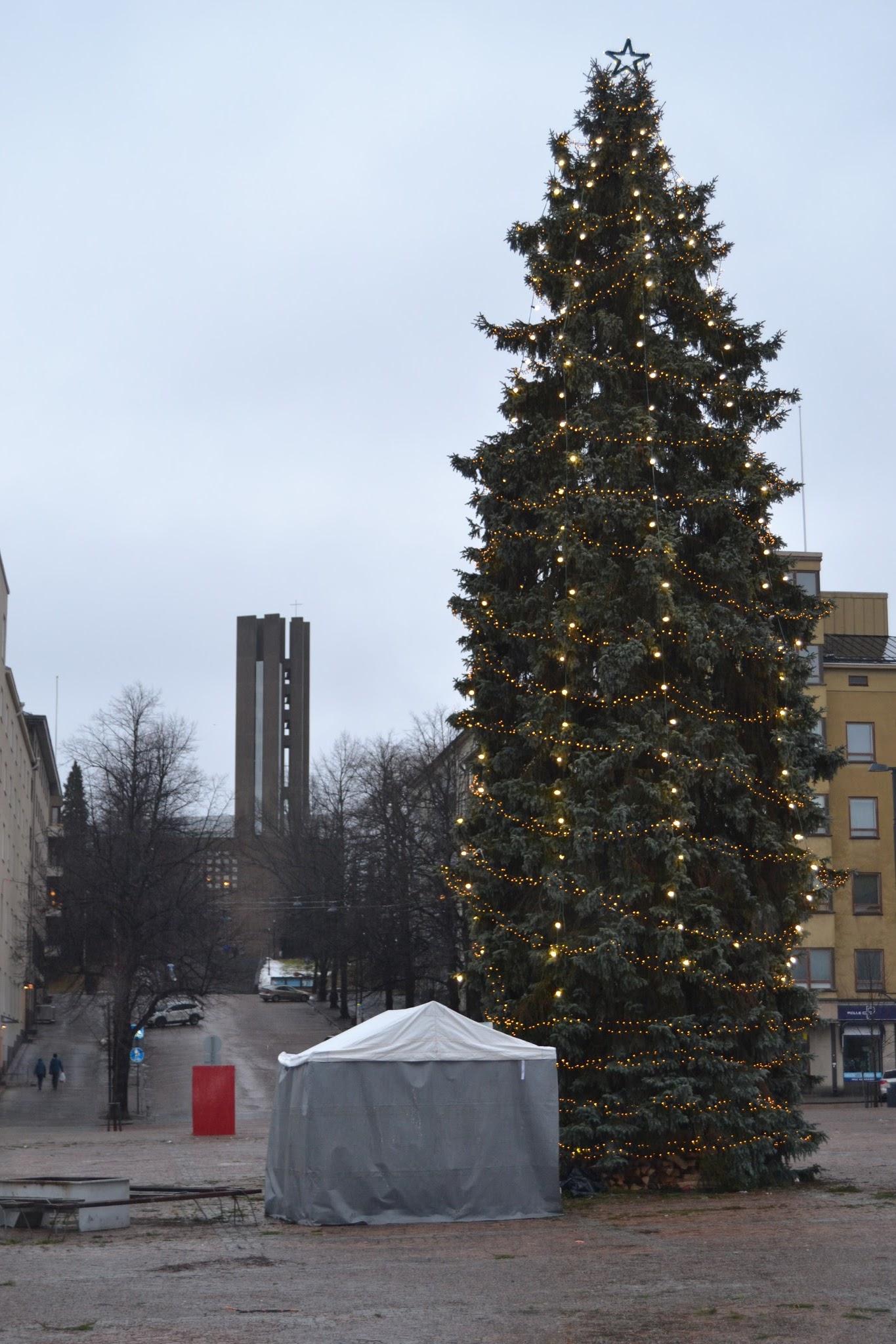 Jouluvaloin koristeltu joulukuusi Lahden torilla, taustalla kirkontorni ja edessä harmaa teltta