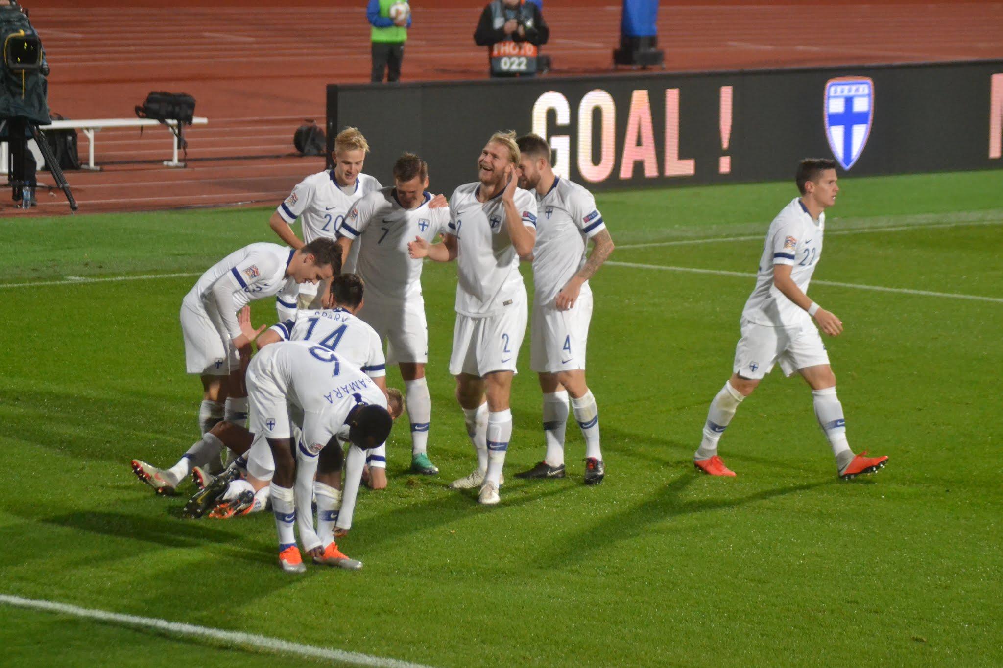 Suomen valkoasuiset pelaajat juhlivat maalia, taustalla mainostaululla teksti GOAL! Suomi–Kreikka-ottelussa