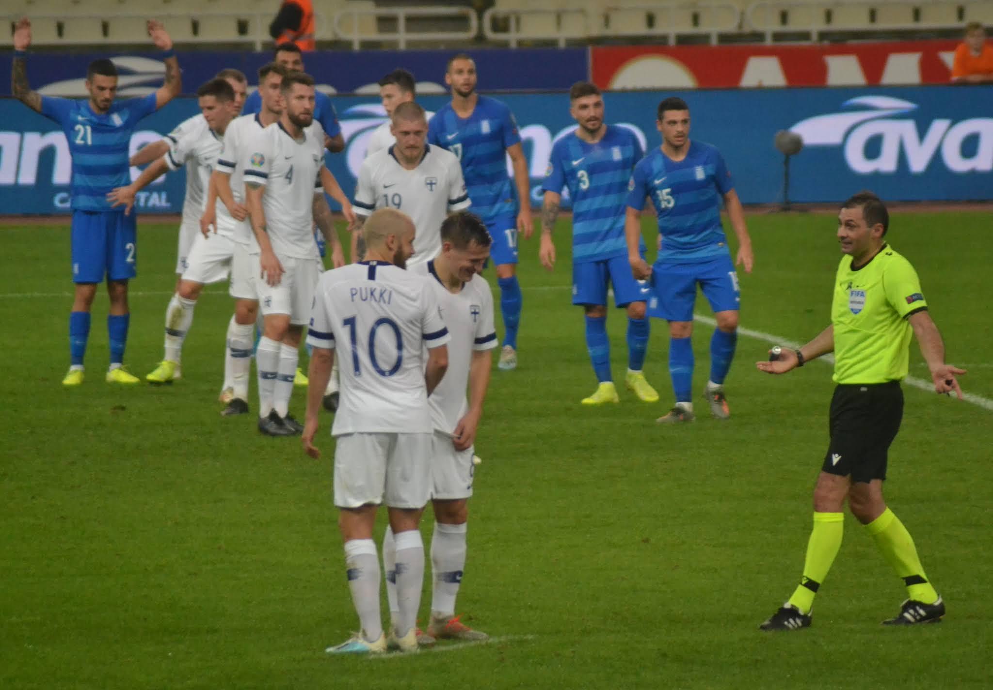 Pukki numero 10 ja joukkuetoveri nauravat, taustalla Kreikan pelaajat ja erotuomari Kreikka–Suomi-ottelussa