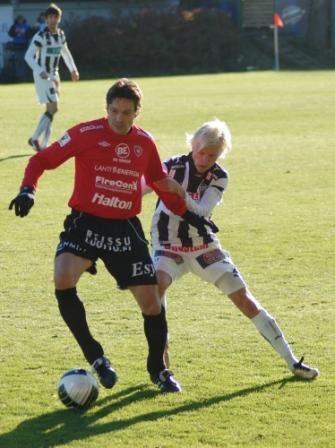 Punapaitainen pelaaja kuljettaa palloa mustavalkoraitaisen vastustajan painostaessa Veikkausliigaottelussa, 23.10.2010