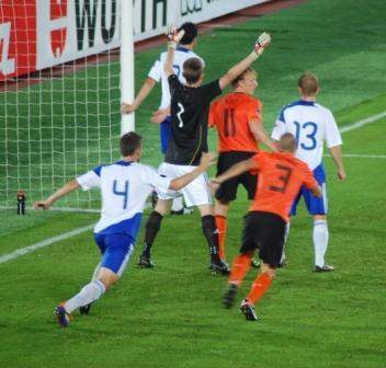 Suomi–Hollanti-ottelussa valko- ja oranssipaitaiset pelaajat maalin edessä, maalivahti kädet ylhäällä, 06.09.2011