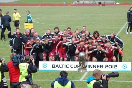 Latvian joukkue juhlii pokaalin kanssa, edessä kyltti Baltic Cup Winner 2012 ja valokuvaajia
