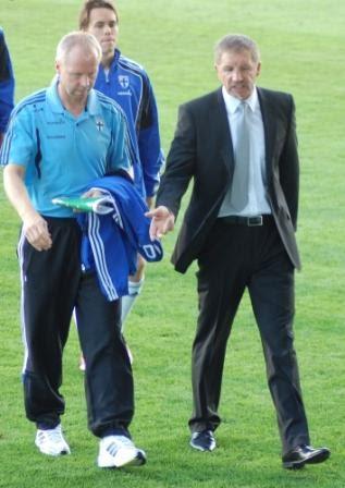 Baxter ja Huttunen kävelevät kentällä, toinen Suomen verryttelyasussa ja toinen puvussa, 11.08.2010