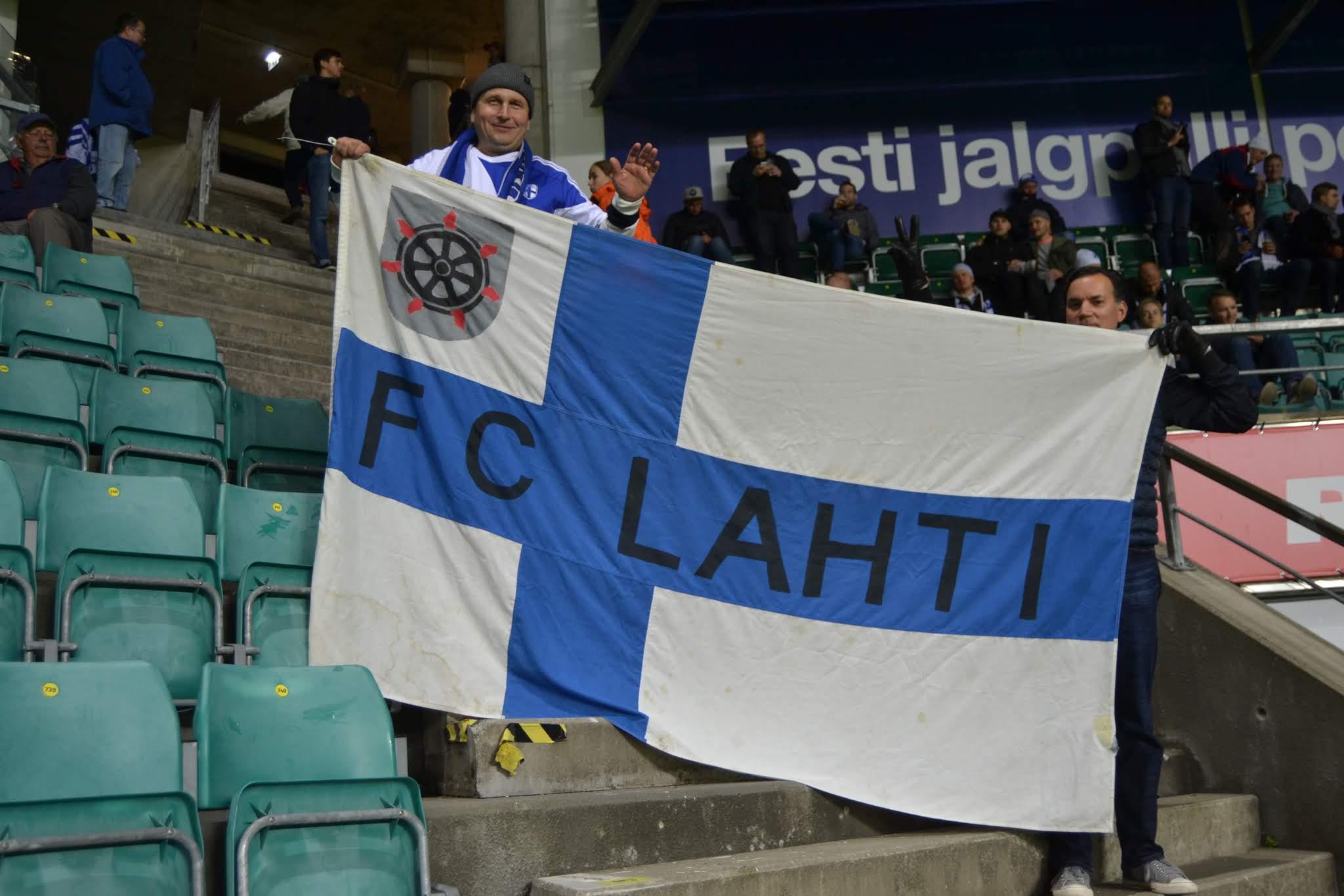 Suomen kannattajat pitelevät FC Lahti -tekstillä varustettua Suomen lippua stadionin katsomossa