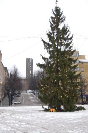 Jouluvaloin koristeltu joulukuusi lumisella torilla, taustalla korkea kirkontorni ja kerrostaloja, 24.12.2011