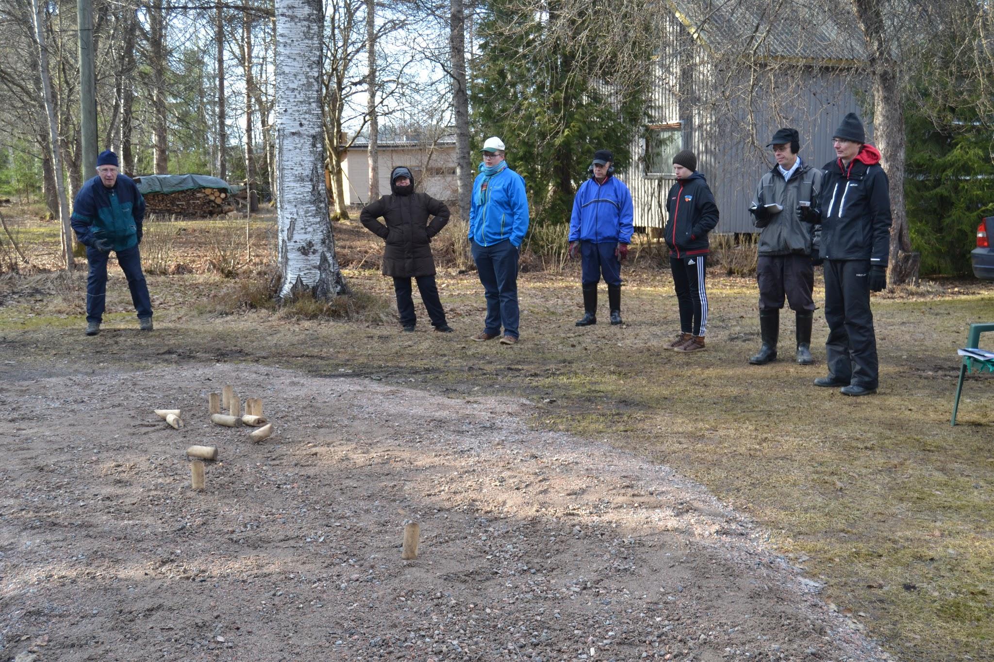Klubilaiset seuraavat mölkkyheittoa soratantereella keväisessä pihapiirissä