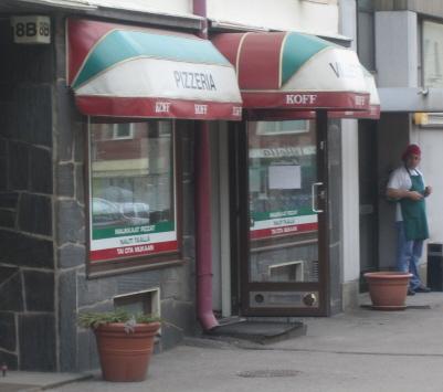 Pizzeria Villettan julkisivu punavalkovihreine markiiseineen, sisäänkäynti ja terrakottaruukut jalkakäytävällä