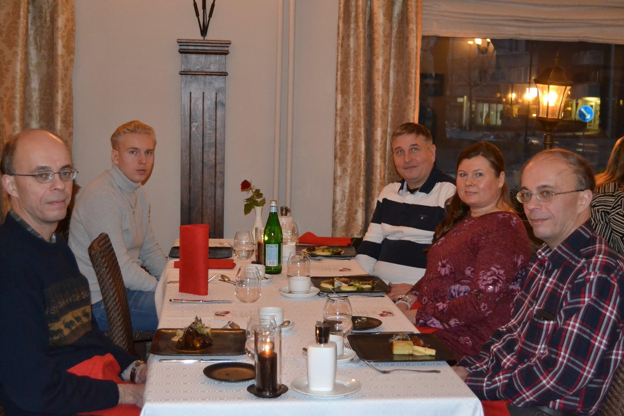Klubilaiset jouluruokailulla valkoisen liinan kattaman pöydän ääressä ravintolassa, ikkunan takana iltavaloja